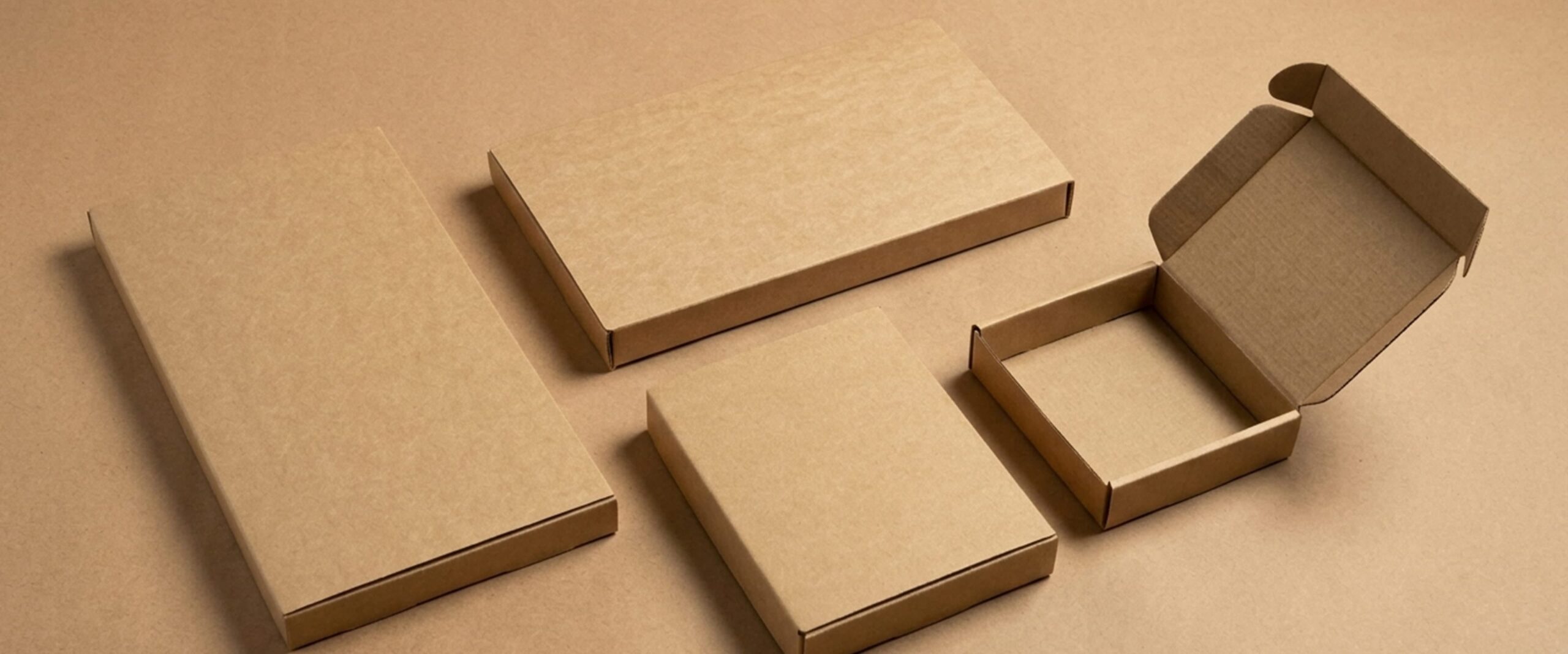 Quatre boîtes en carton brun de différentes tailles posées à plat sur un fond assorti, dont une ouverte montrant l'intérieur.