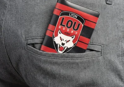 Portefeuille rouge et noir à logo LOU Lyon Rugby avec tête de loup dépassant d'une poche arrière de pantalon gris.