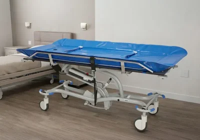 Brancard d'hôpital réglable sur roulettes avec matelas bleu imperméable installé dans une chambre au sol en bois.