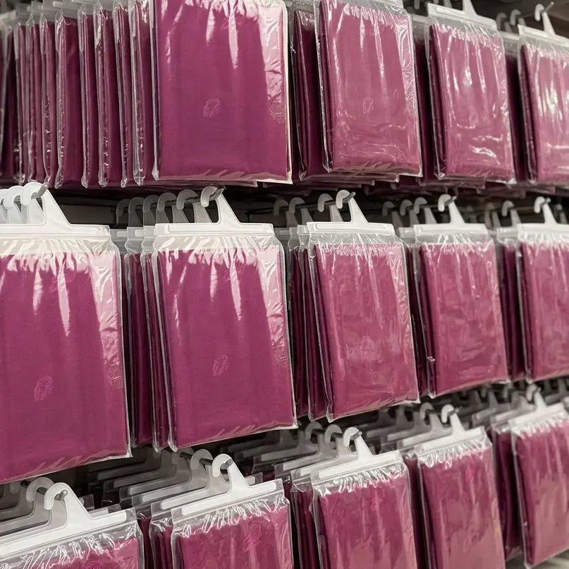 Rangées de pochettes plastiques suspendues contenant des foulards ou tissus de couleur rose foncé, emballés individuellement.