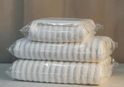 Trois serviettes blanches à rayures empilées et emballées sous film plastique transparent, sur une surface claire.