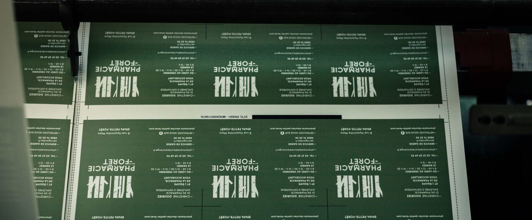 Feuille verte imprimée en répétition avec texte blanc «PHARMACIE FORET» et repères de coupe, rouleau d'imprimante visible.