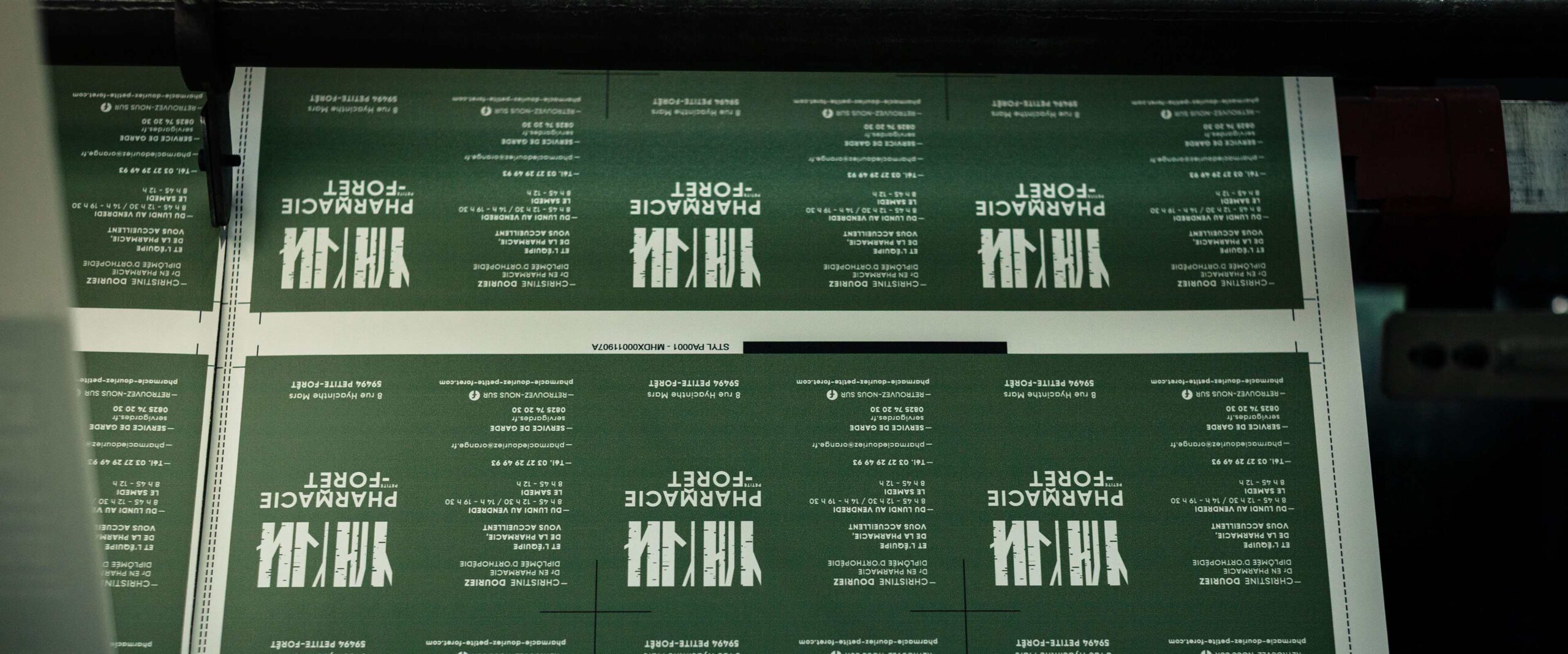 Feuille verte imprimée en répétition avec texte blanc «PHARMACIE FORET» et repères de coupe, rouleau d'imprimante visible.