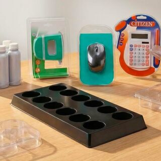 Plateau noir à 10 alvéoles entouré de contenants plastiques transparents, flacons blancs et emballages d'articles électroniques sur une table en bois.