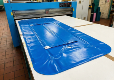Grande housse bleue en PVC avec sangles et boucle blanche, posée sur une table de coupe industrielle dans un atelier.