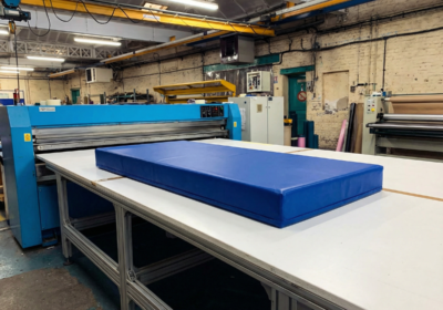 matelas rectangulaire bleu posé sur une grande table de coupe dans un atelier de fabrication avec machines industrielles en arrière-plan.