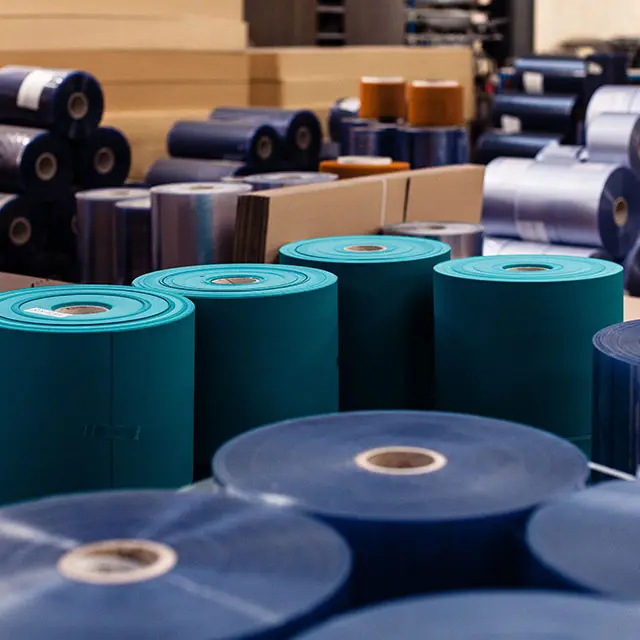 Rouleaux de film plastique et matériaux d'emballage empilés en bobines de différentes couleurs dans un entrepôt.